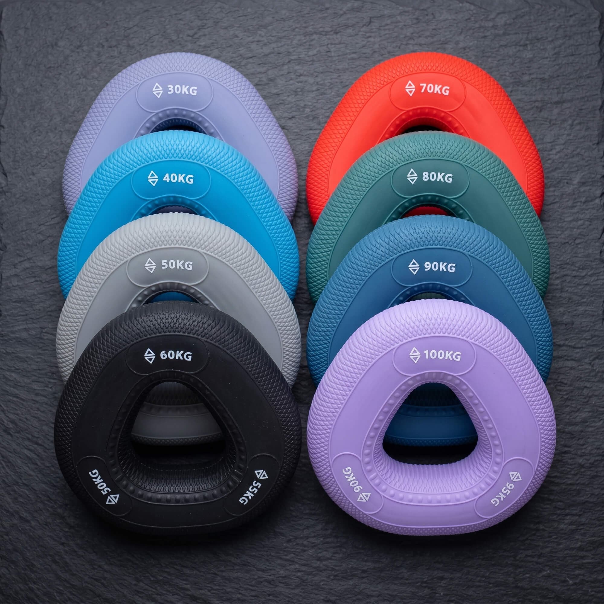 Dad Hands grip rings fanned in two stacks on slate, 30kg to 100kg